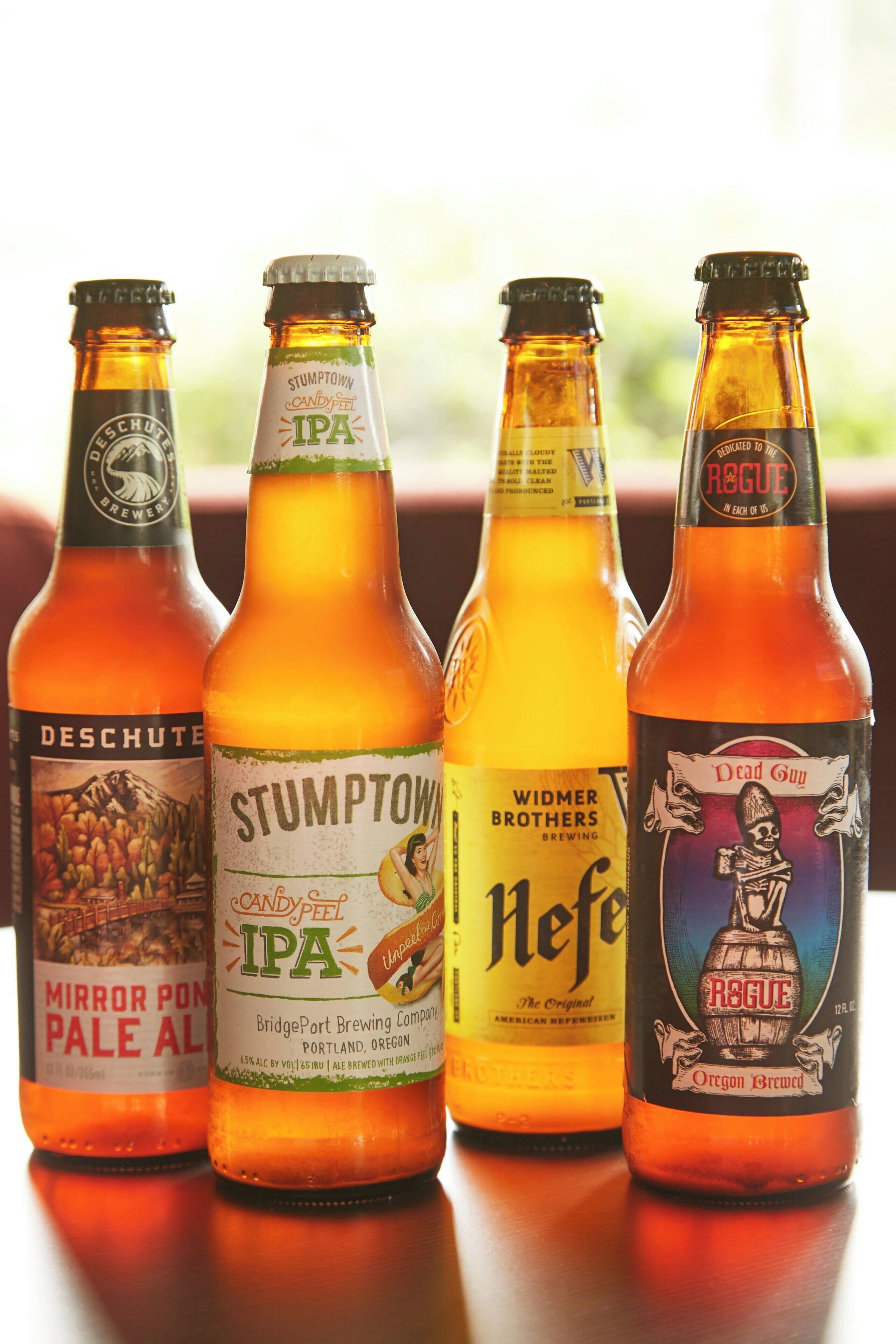 Four beer bottles with labels on a reflective surface.