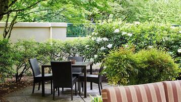 An outdoor patio with a table and chairs, surrounded by lush greenery and a striped sofa.