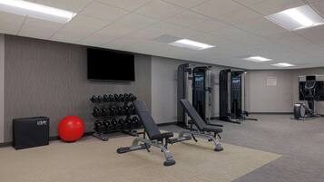 Ein Fitnessraum mit Kraftgeräten, einem roten Trainingsball und einem an der Wand montierten Fernseher.