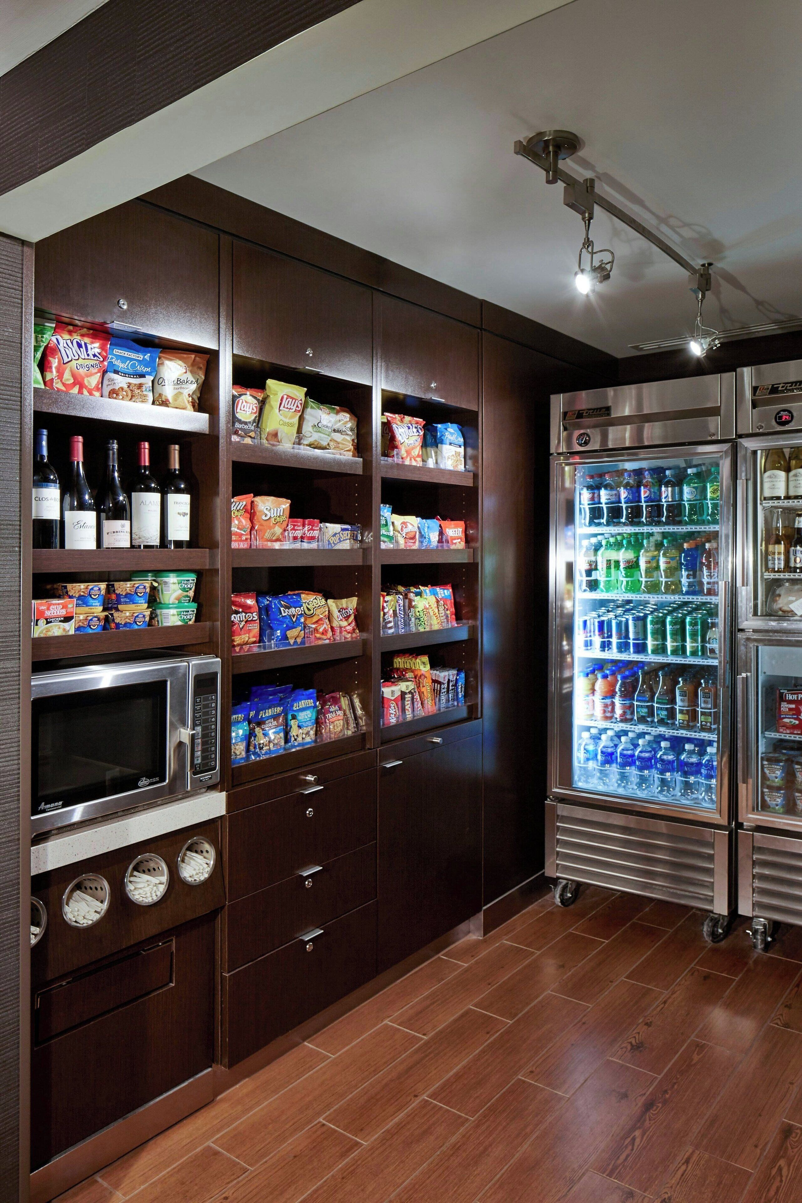 A kitchen with built-in appliances, including a microwave, oven, and refrigerator, and shelves stocked with snacks and beverages.