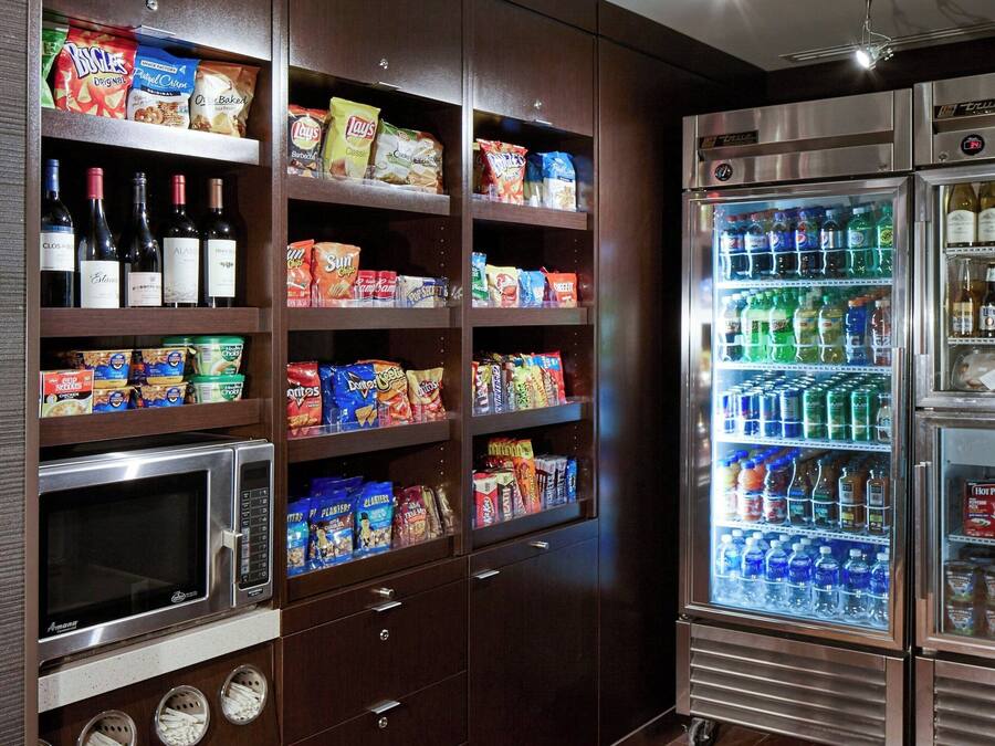 A kitchen with built-in appliances, including a microwave, oven, and refrigerator, and shelves stocked with snacks and beverages.