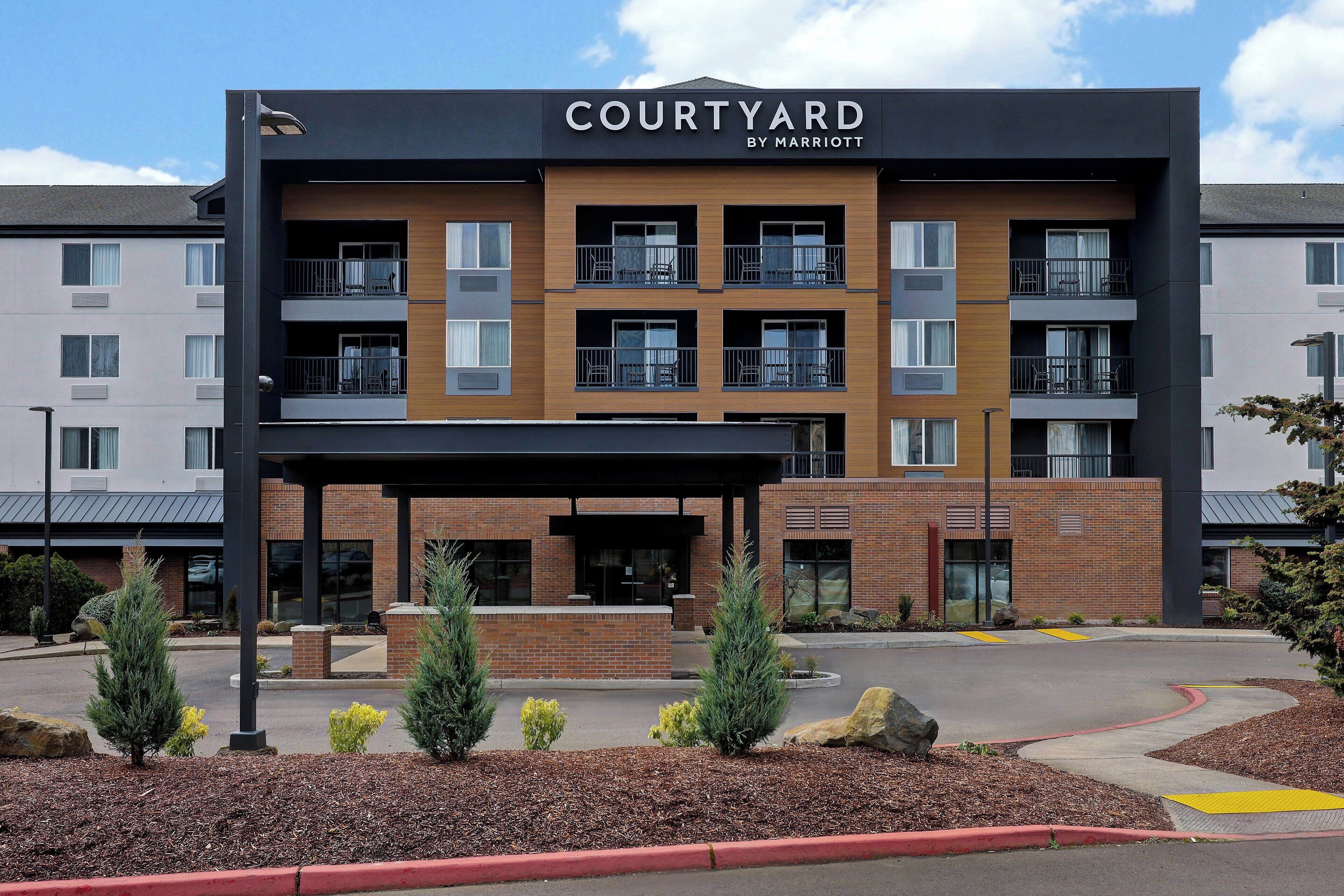 A multi-story Courtyard by Marriott hotel with a modern design, featuring balconies, a covered entrance, and landscaped surroundings.