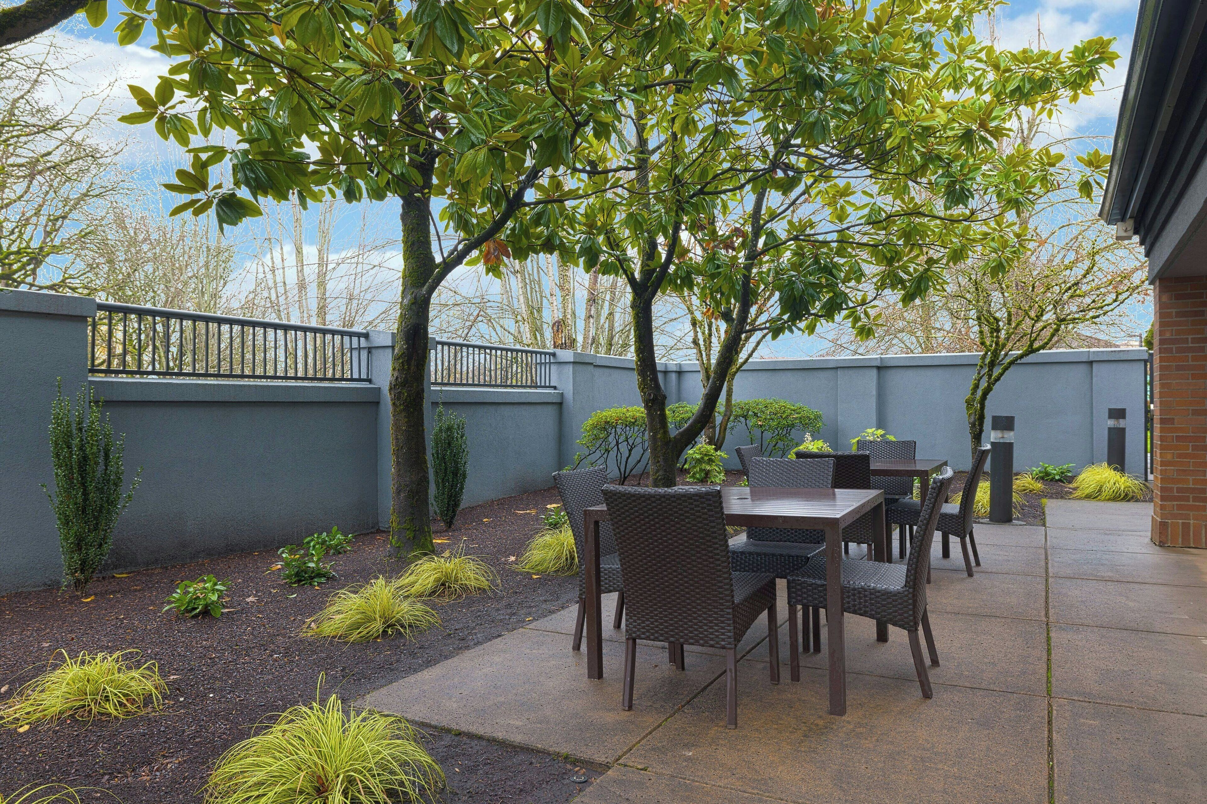 An outdoor patio with a table and chairs, surrounded by a low brick wall and a metal fence.