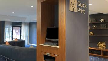 A modern hotel lobby with a curved seating area, a printer station, and a bookshelf with decorative items.