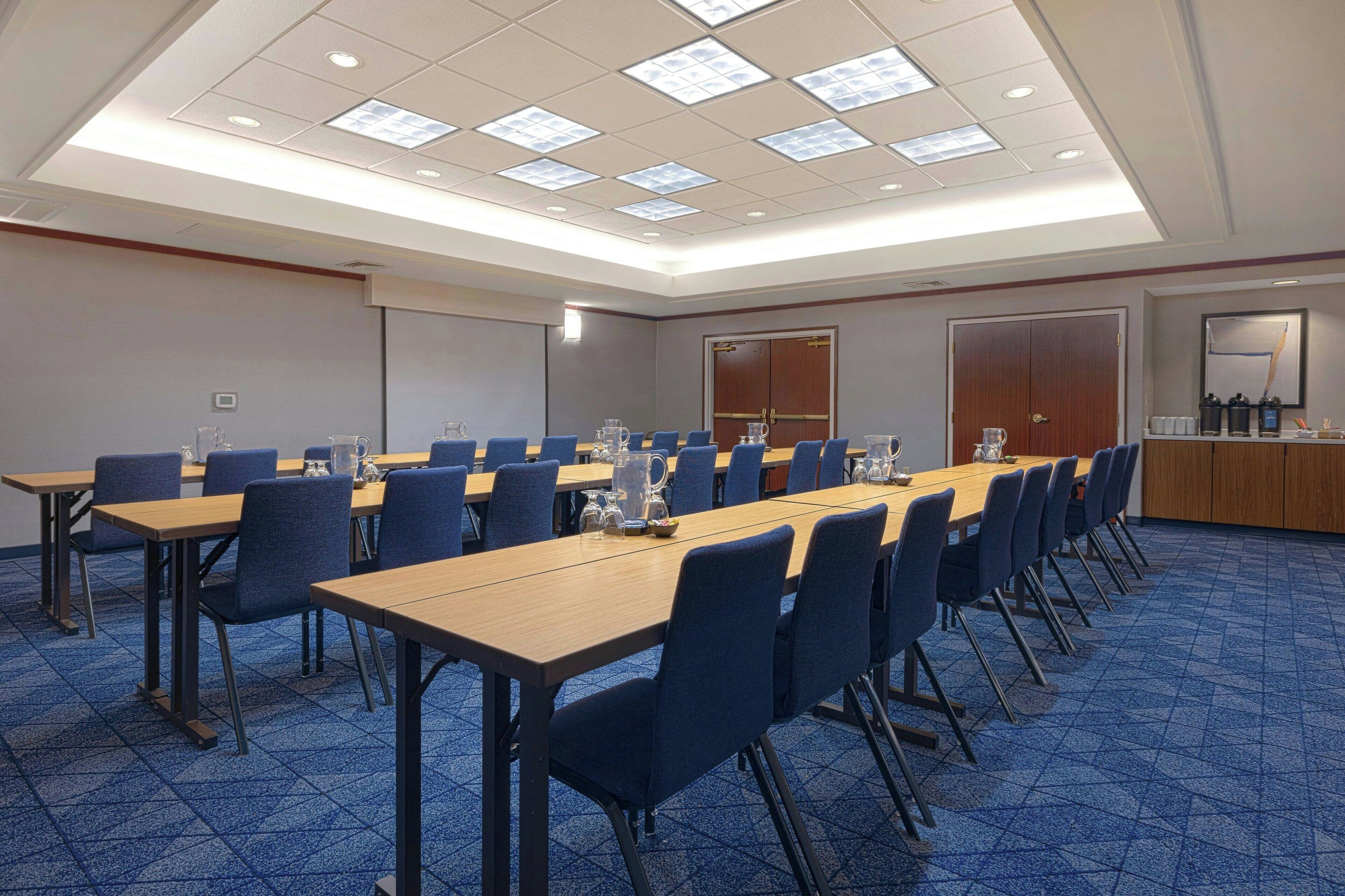 Un salón de conferencias con mesas largas, sillas azules y alfombra azul.