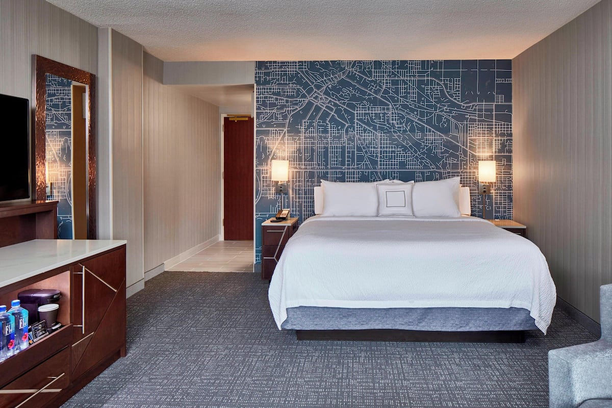 Hotellihuone, jossa on suuri sänky, taulutelevisio, peilillä varustettu työpöytä ja seinä, jossa on kaupungin karttakuvio.
