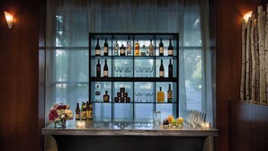 A bar area with shelves of bottles and glasses, a bar counter, and a window with curtains. - Courtyard Portland Downtown/Convention Center (Portland)
