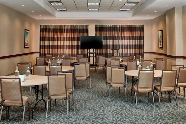A hotel conference room with multiple tables and chairs, a large flat-screen TV, and striped curtains. - Courtyard Portland Downtown/Convention Center (Portland)