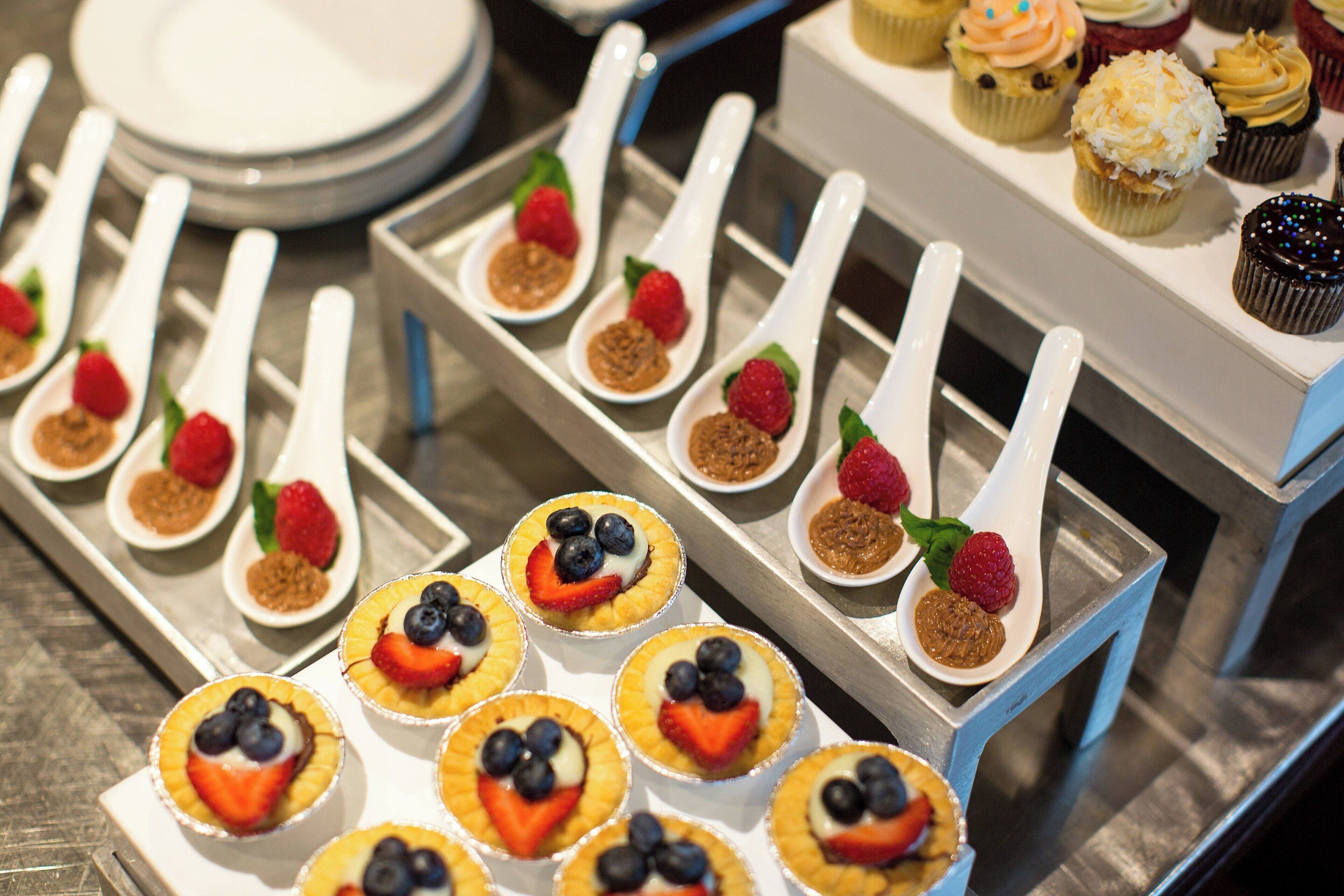 Un bufé con diversos postres, incluyendo cupcakes y tartaletas con frutas.