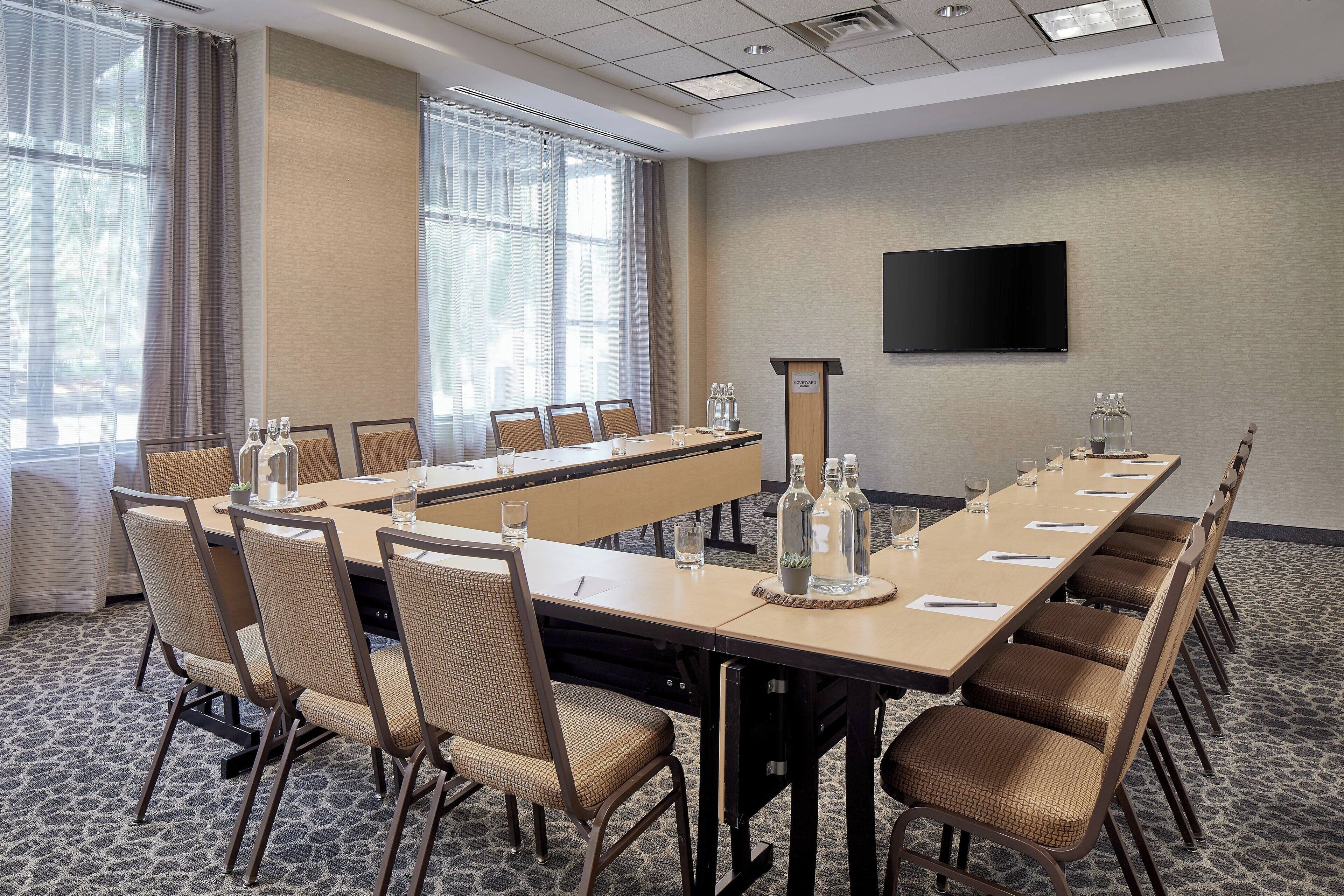 A conference room with a long table, chairs, a podium, and a TV on the wall.