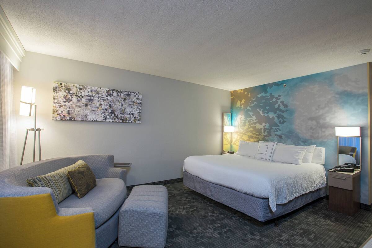 A hotel room with a bed, a sofa, a small table, and a wall with a large abstract painting.