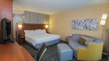 A hotel room with a bed, a sofa, a desk, a TV, and a lamp.