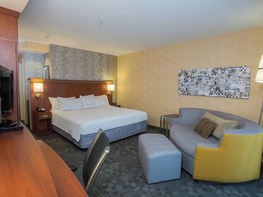 A hotel room with a bed, a sofa, a desk, a TV, and a lamp.