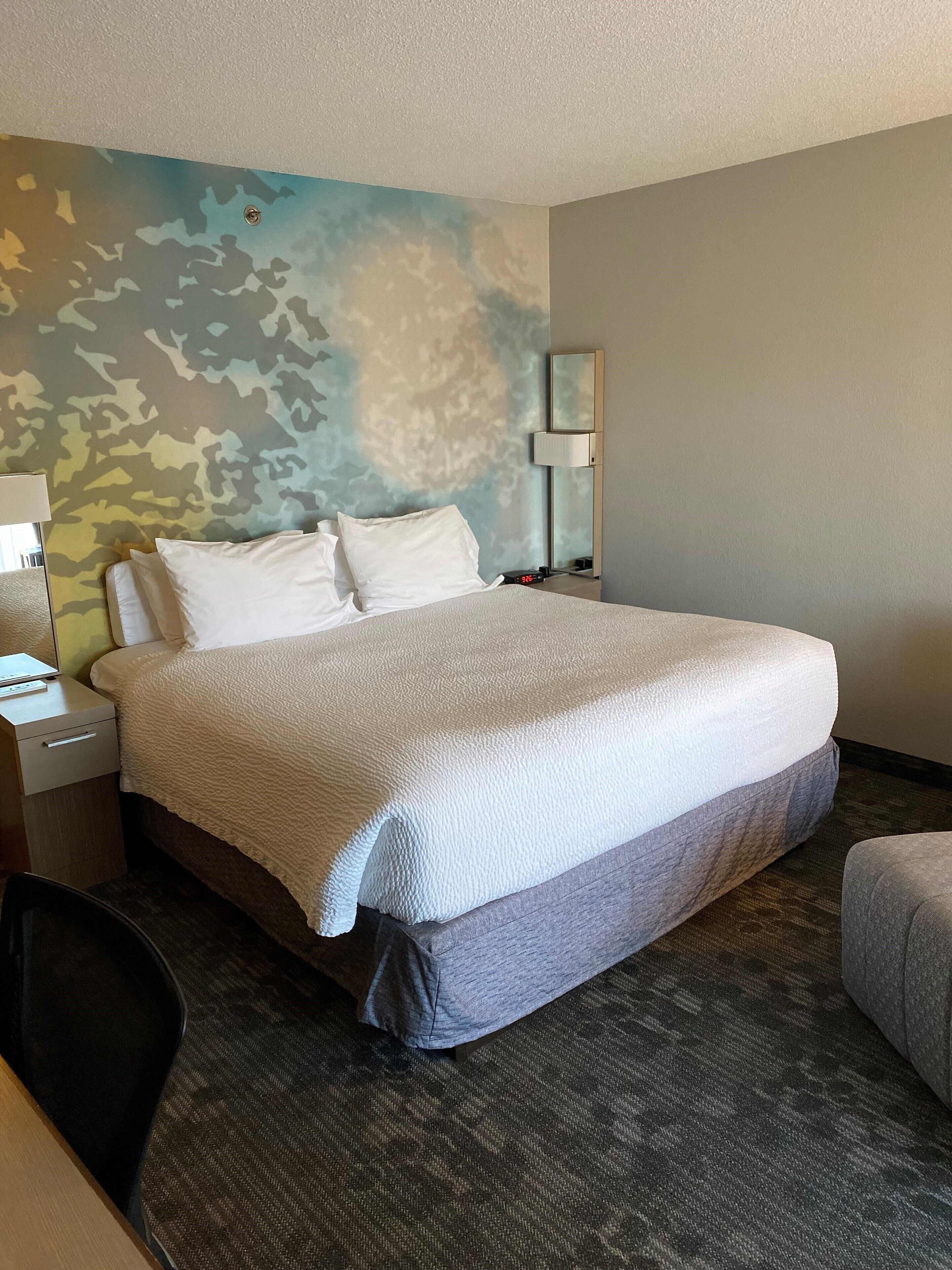 Une chambre d’hôtel avec un grand lit, une table de chevet, un bureau, une chaise et un mur orné d’un motif de camouflage.