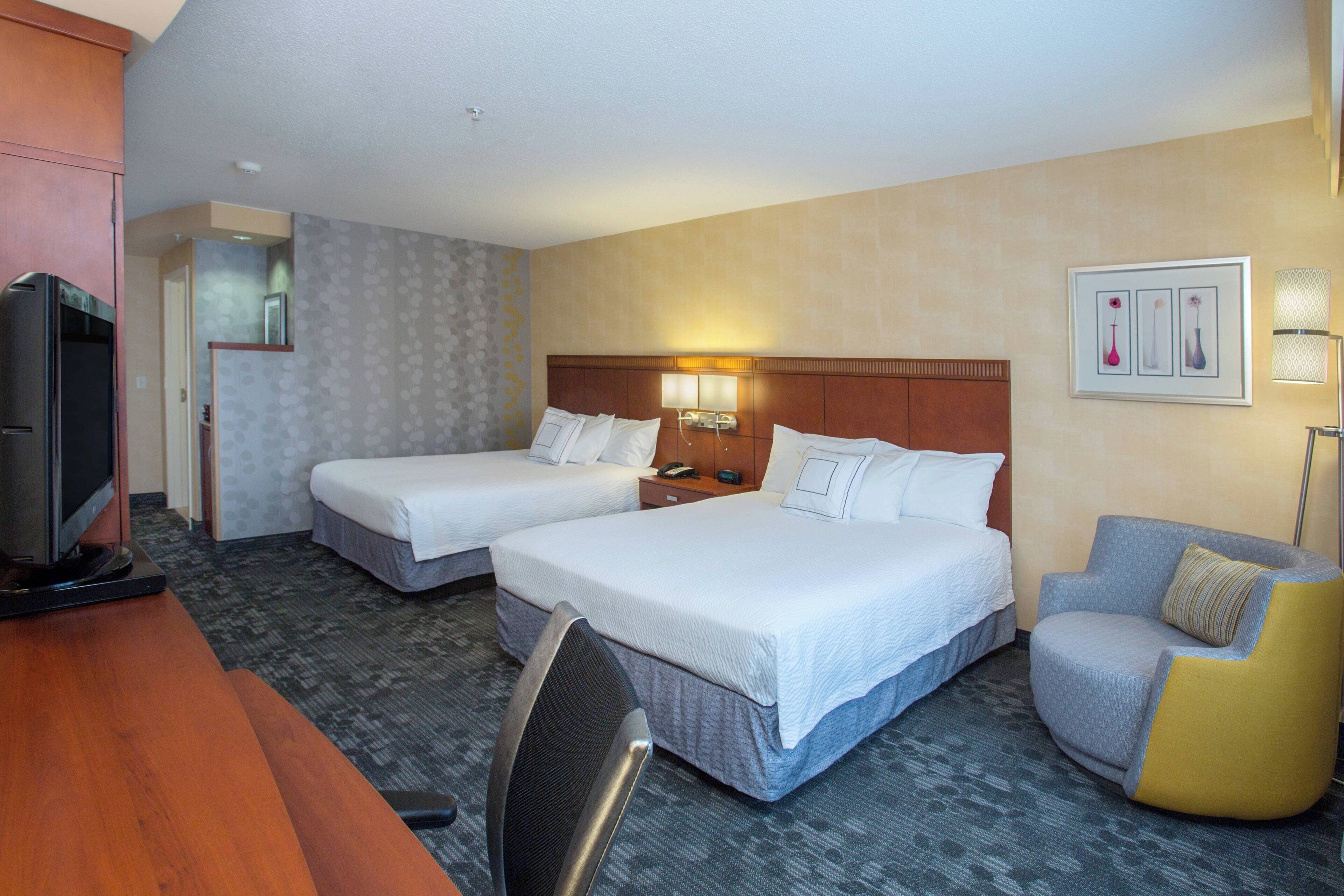 A hotel room with two beds, a desk with a television, a chair, and a lamp.