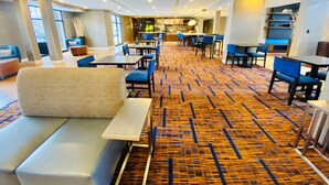 Un hall d’hôtel avec un tapis à motifs, des espaces aménagés pour s’asseoir et un bar en arrière-plan.