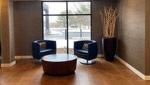 Un hall d’entrée avec deux fauteuils bleus, une table basse en bois et une grande fenêtre donnant sur l’extérieur.
