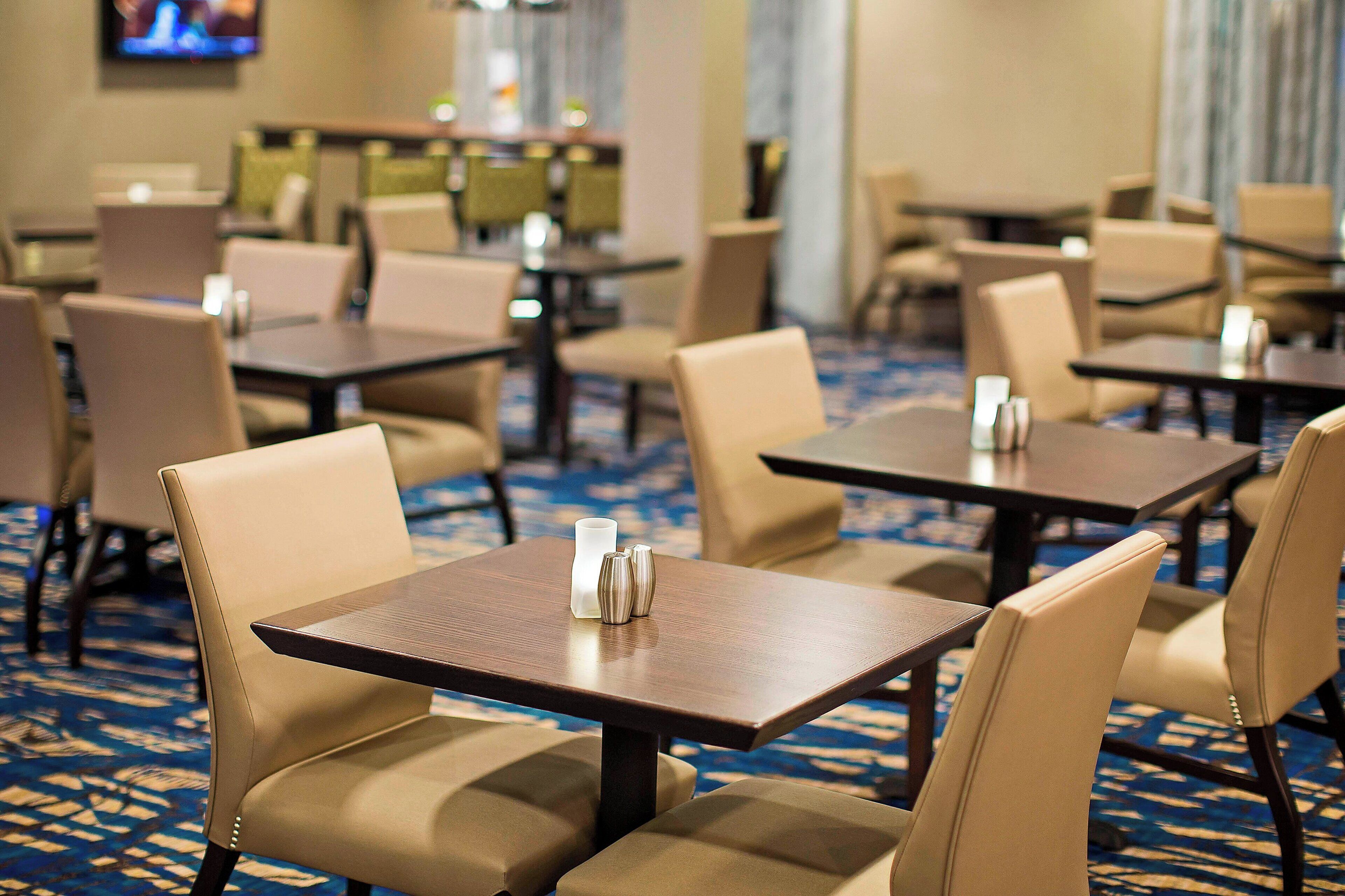 Une salle à manger d'hôtel avec plusieurs tables et chaises, un sol recouvert de moquette et un téléviseur fixé au mur.