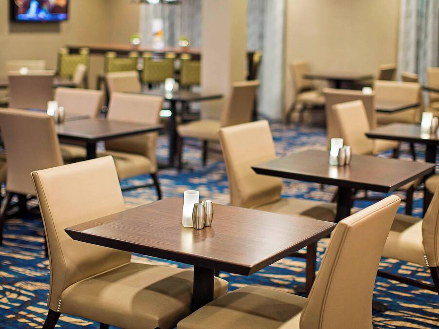 Une salle à manger d'hôtel avec plusieurs tables et chaises, un sol recouvert de moquette et un téléviseur fixé au mur.