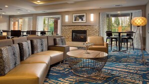 A modern living room with a fireplace, a round coffee table, and a sofa with patterned cushions. - Courtyard by Marriott North Seattle/Lynnwood (Lynnwood)