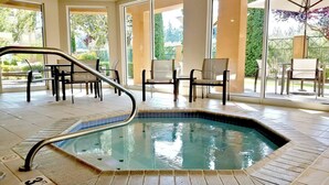 A swimming pool with a metal handrail, surrounded by chairs and tables, with large windows offering views of greenery. - Courtyard by Marriott North Seattle/Lynnwood (Lynnwood)