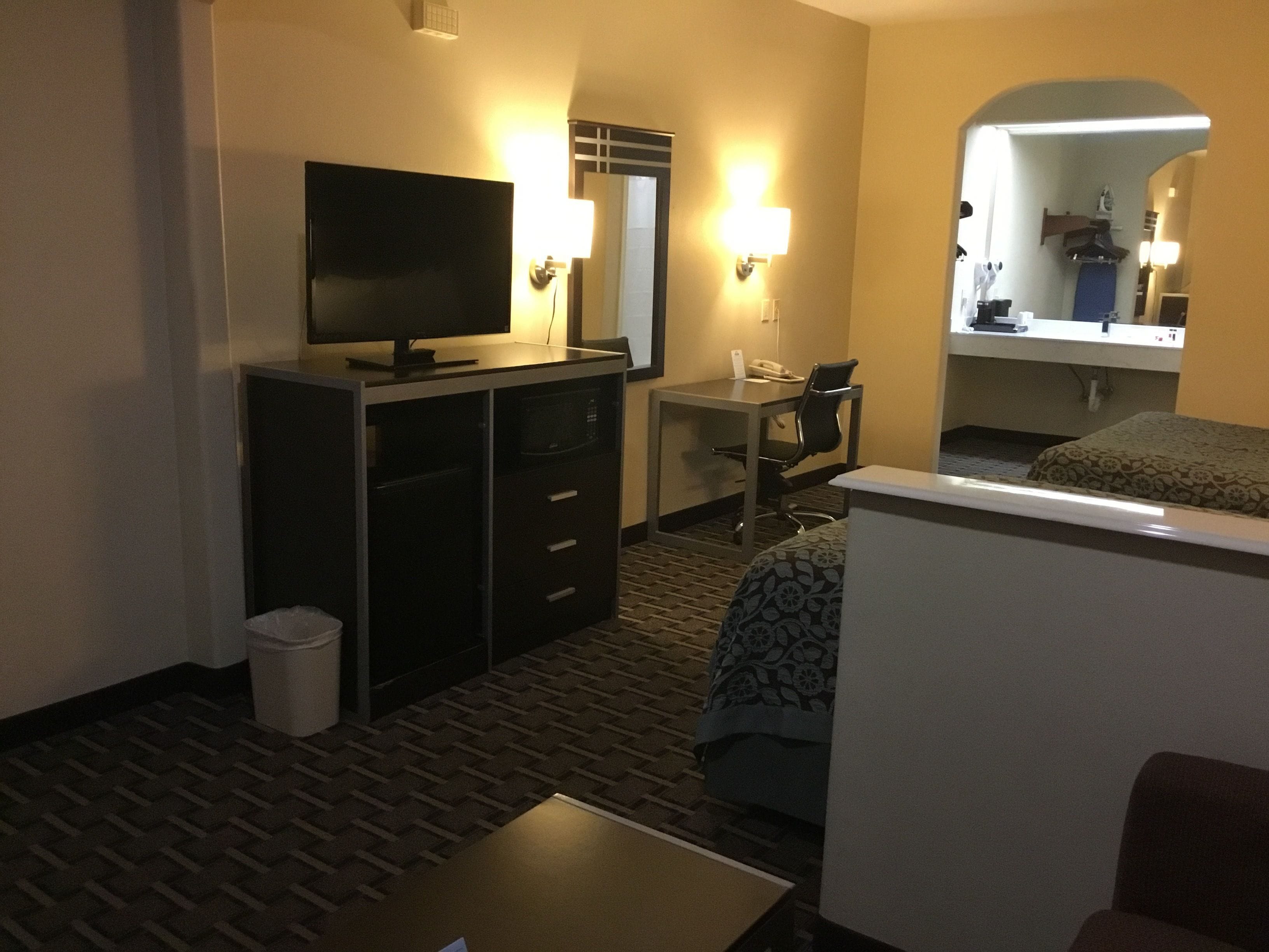 A hotel room with a bed, a desk, a chair, a television, and a small trash bin.