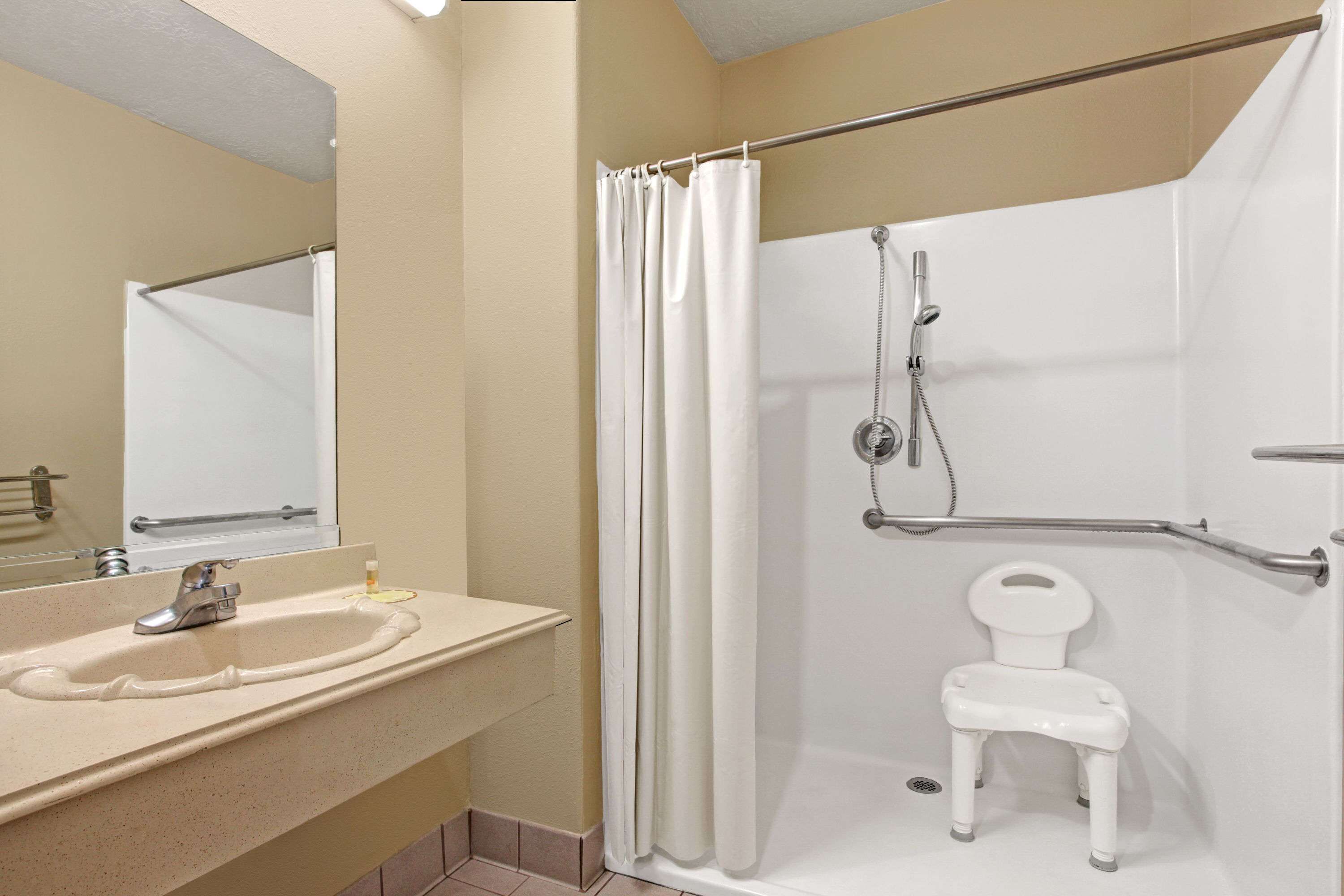 A bathroom with a sink, mirror, shower, and a white chair.