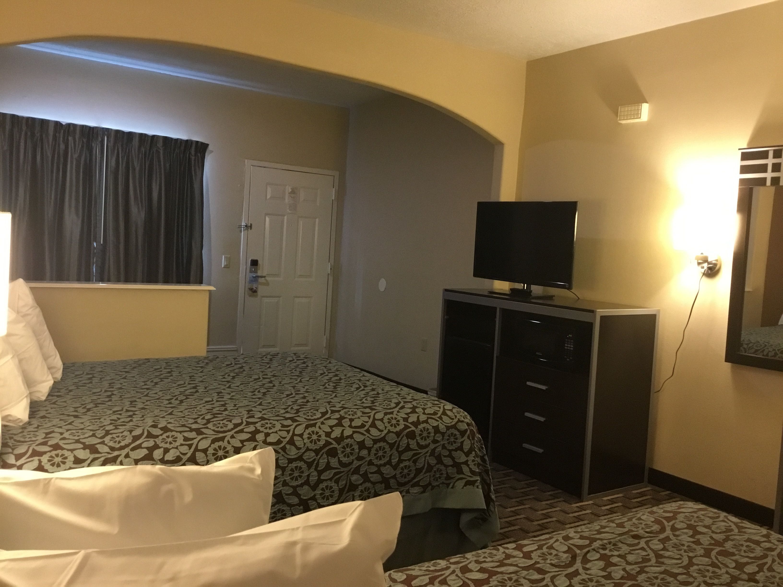 Habitación de hotel con dos camas, un televisor sobre un mueble, una puerta y una alfombra estampada.