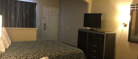 A hotel room with two beds, a television on a stand, a door, and a patterned carpet.