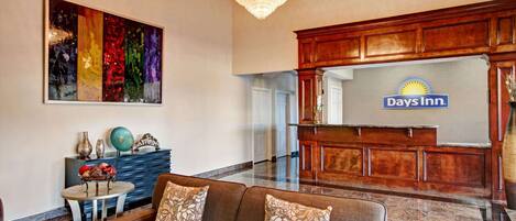 A lobby with a brown sofa, a chandelier, a Days Inn sign, and a colorful abstract painting.