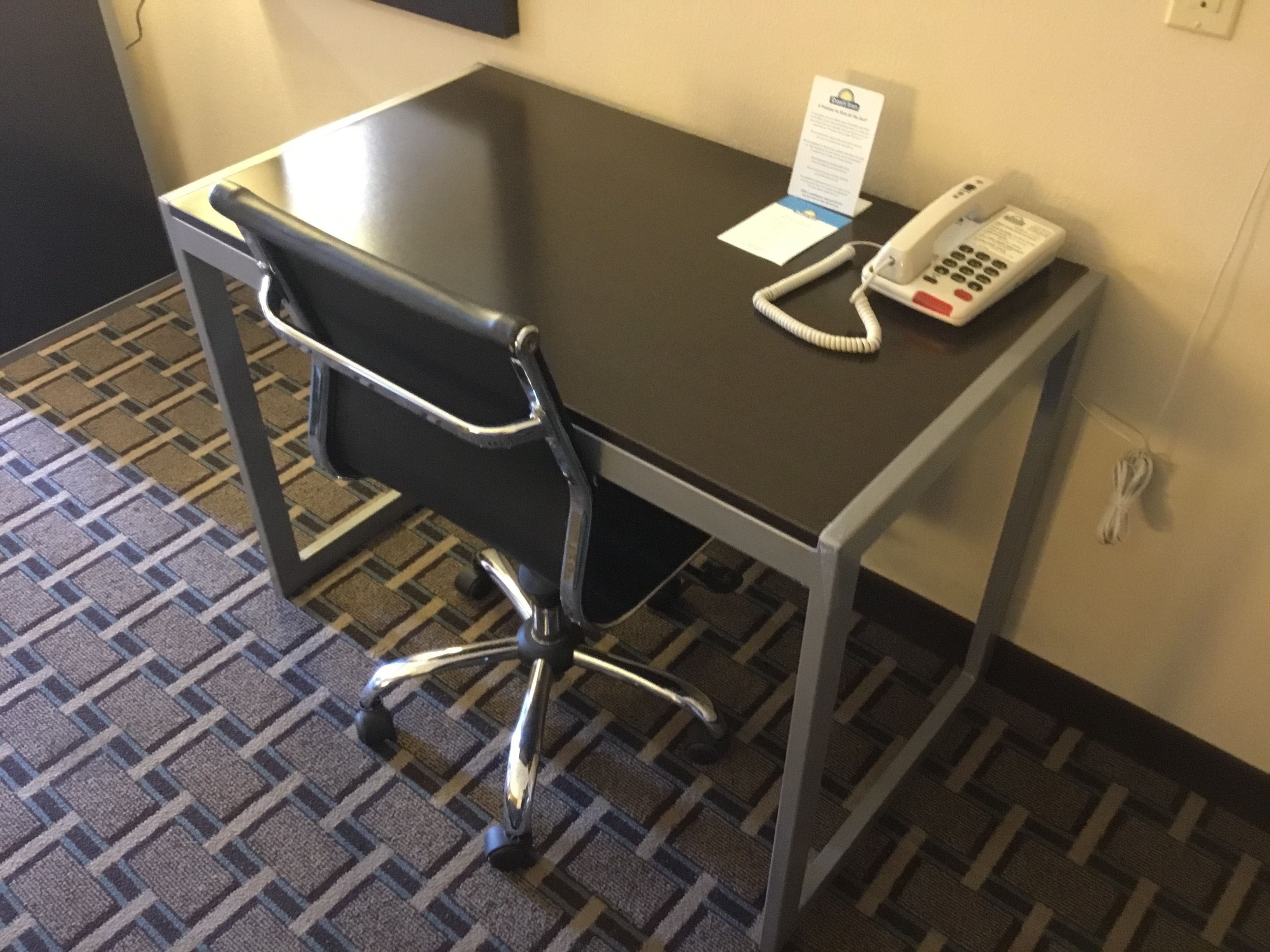 A hotel room with a black office chair, a desk, and a telephone.