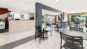 A hotel lobby with a reception desk, a seating area with tables and chairs, and a view of the outdoors.