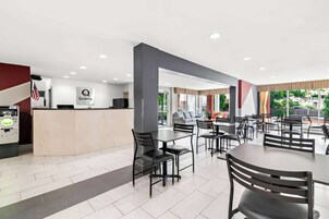 Vestíbulo de hotel con mostrador de recepción, una zona de estar con mesas y sillas, y vistas al exterior.