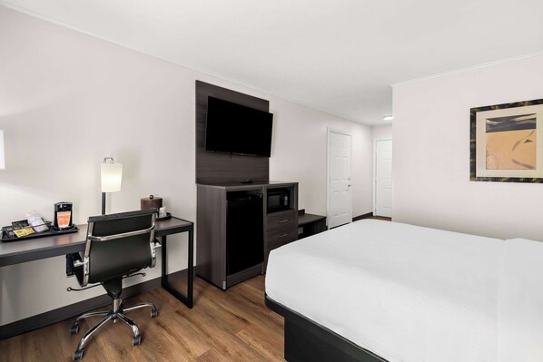 Habitación de hotel con cama, escritorio, silla, televisión, microondas y puerta.