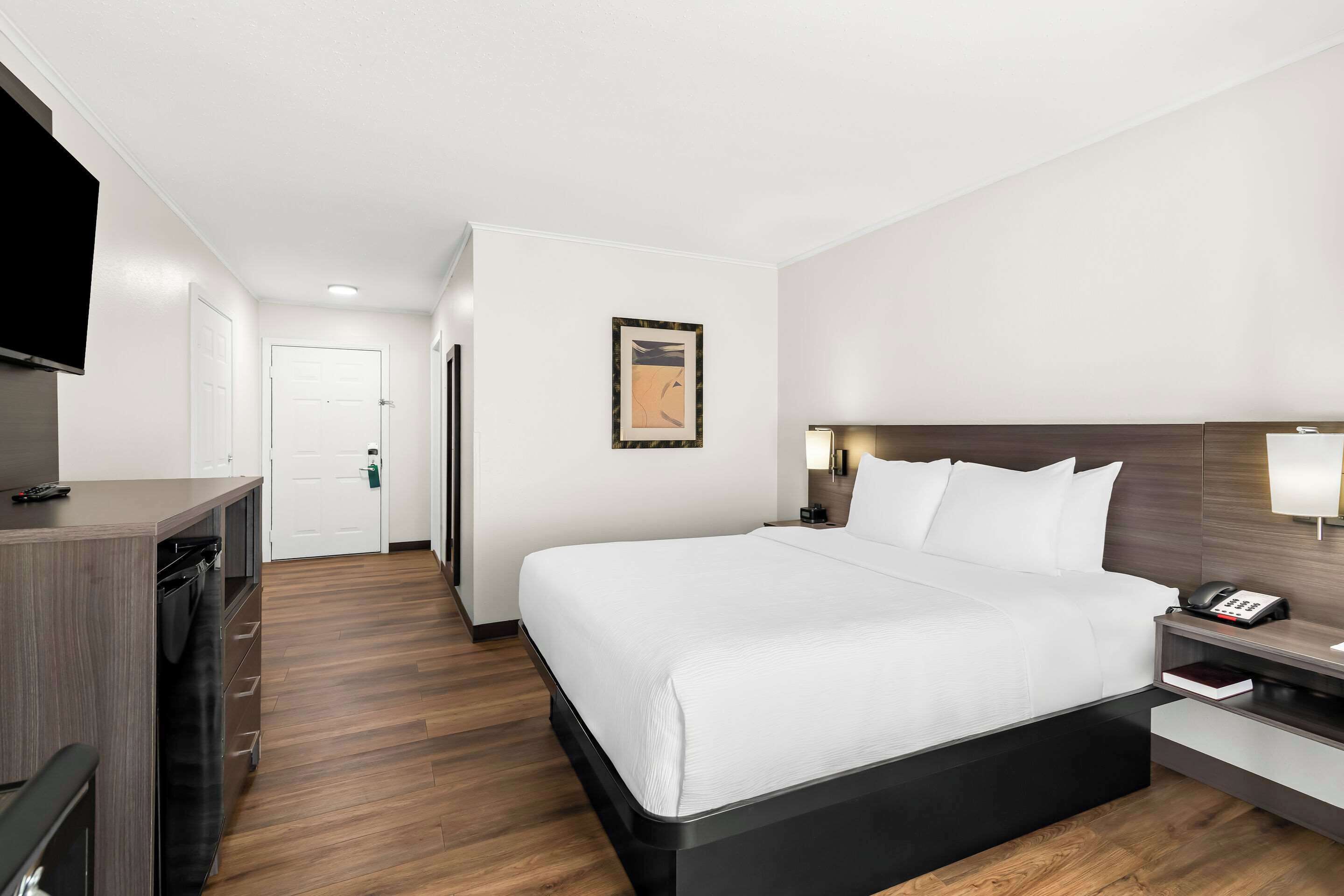 Habitación de hotel con una cama grande, mesita de noche con lámpara, televisión instalada en la pared y suelo de madera.