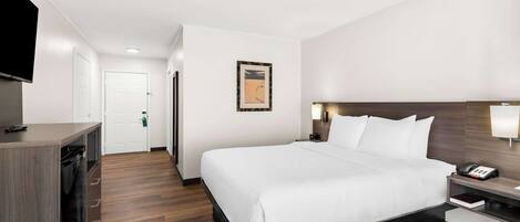 Habitación de hotel con una cama grande, mesita de noche con lámpara, televisión instalada en la pared y suelo de madera.
