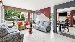 A modern hotel lobby with a large American flag, comfortable seating, a dining area, and a TV screen.