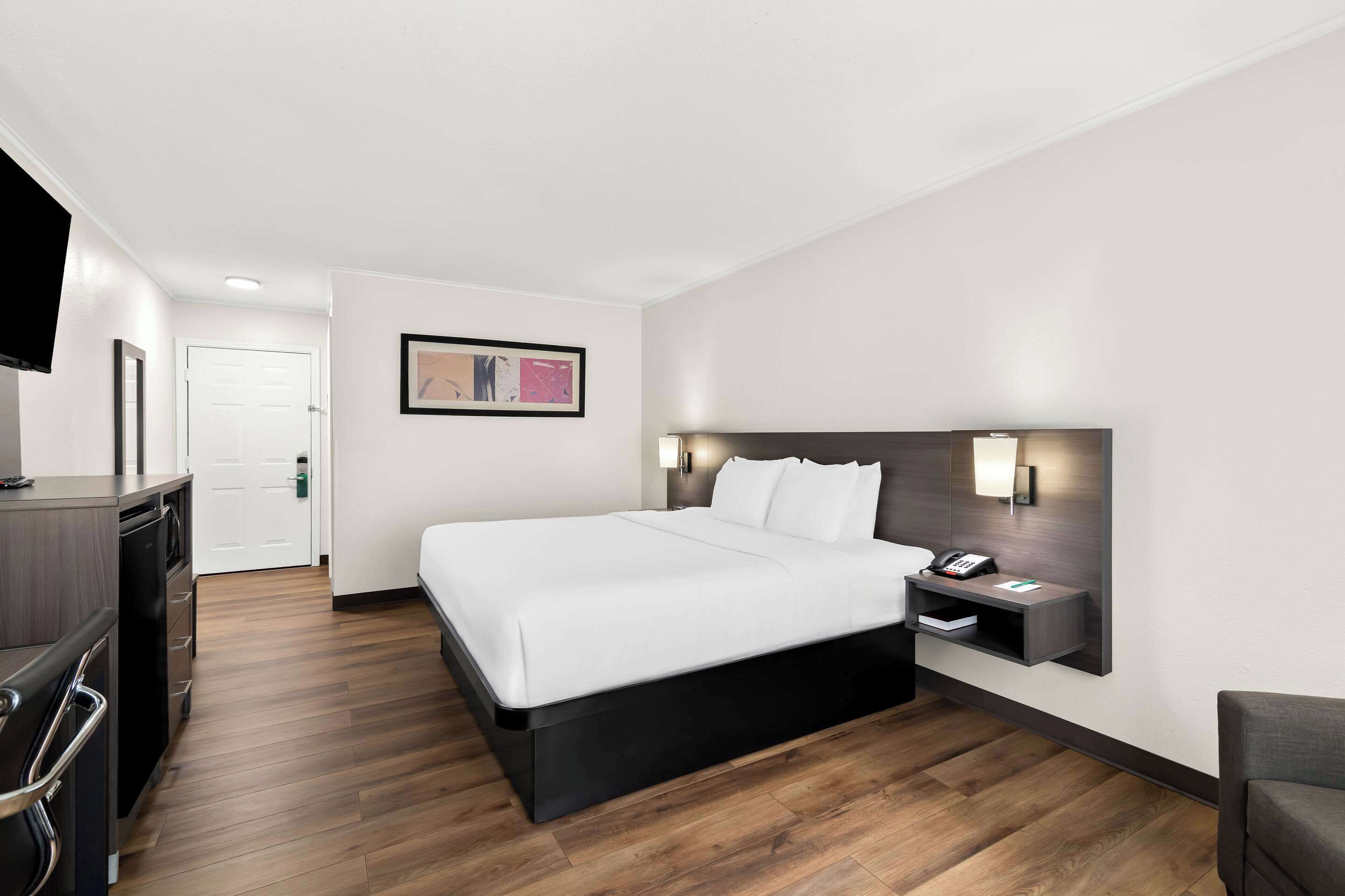 Une chambre d’hôtel moderne avec un grand lit, un bureau avec un téléphone et un téléviseur fixé au mur.