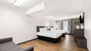 A modern hotel room with a bed, a sofa, a desk, and a flat-screen TV.