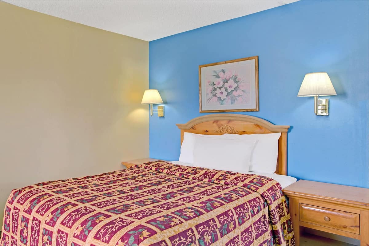A bedroom with a bed, two bedside lamps, a nightstand, and a framed floral artwork on the wall.