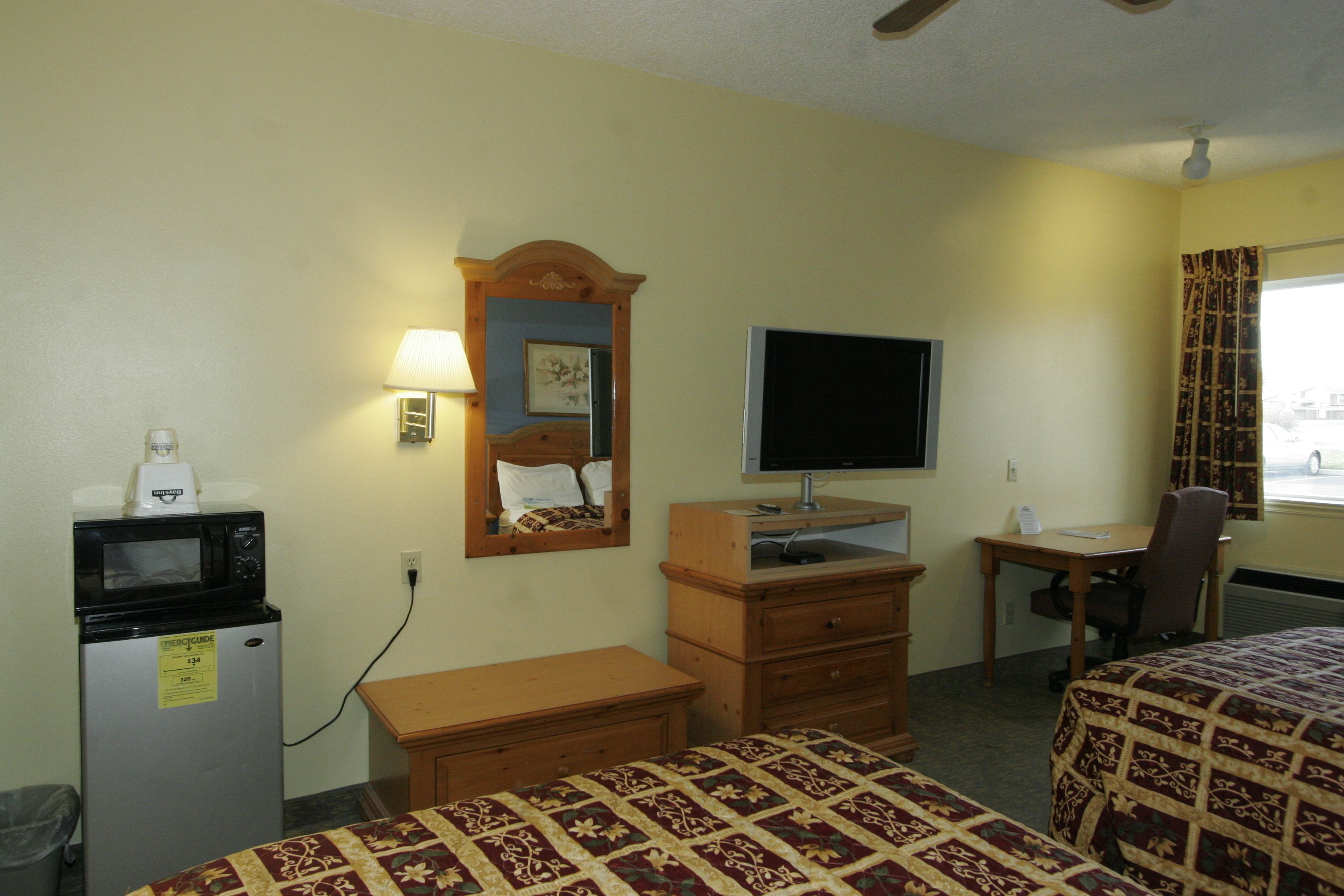 A hotel room with two beds, a desk, a chair, a television, a microwave, and a small refrigerator.