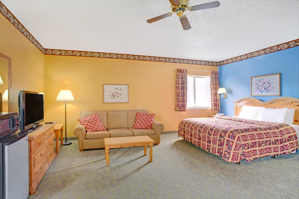 A hotel room with a bed, a sofa, a TV, a desk, and a ceiling fan.