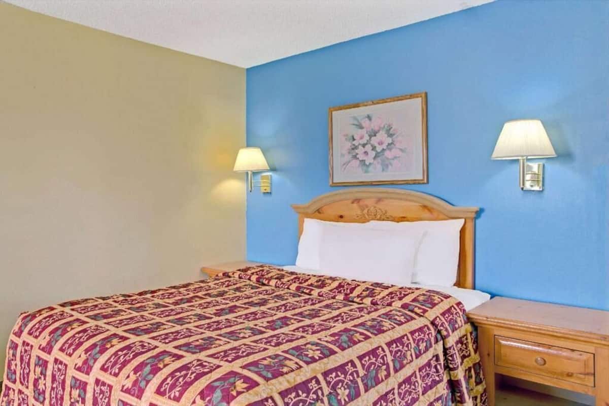 A hotel room with a bed, two bedside lamps, a nightstand, and a framed floral artwork on the wall.