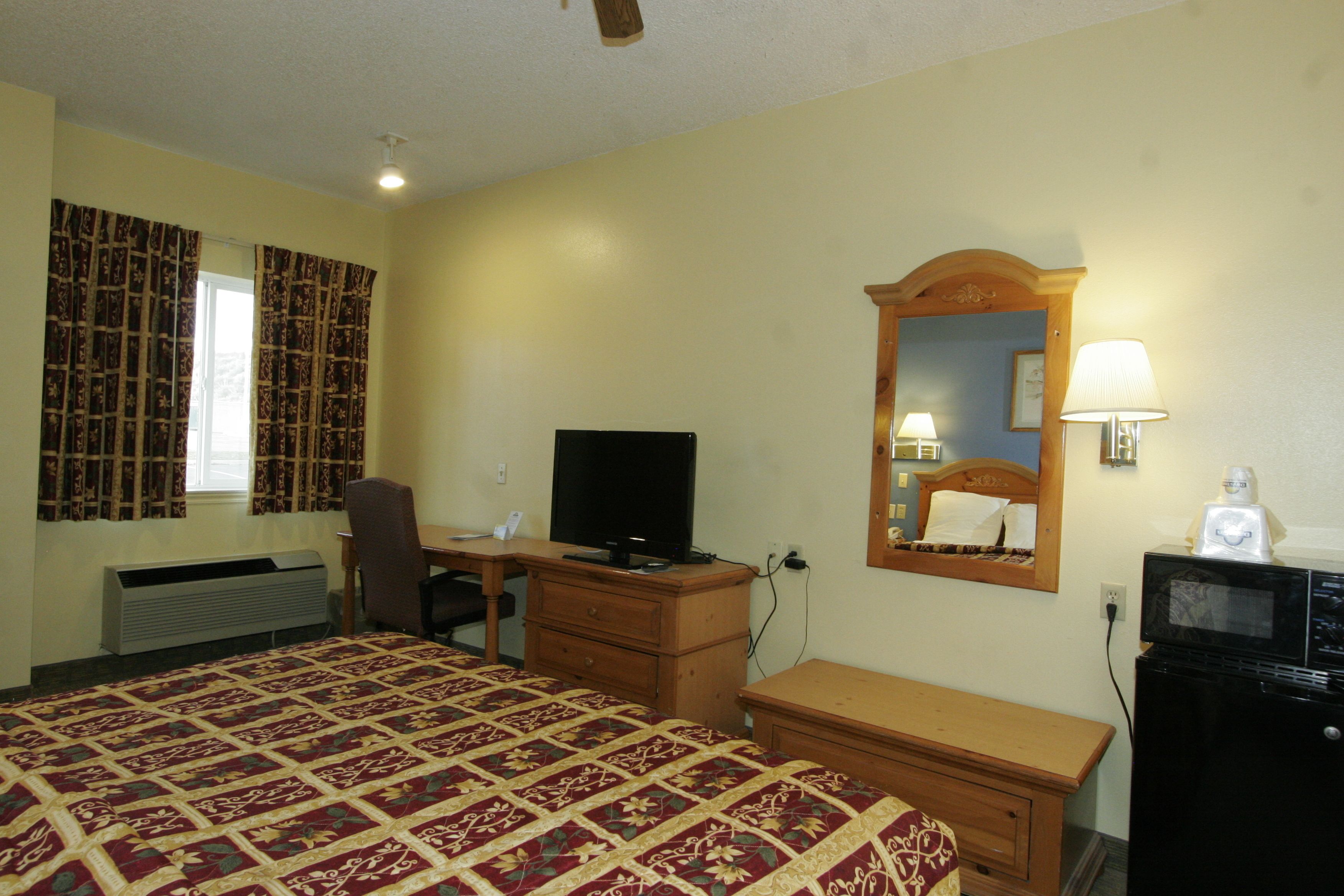 A hotel room with a bed, desk, chair, dresser, television, mirror, and microwave.