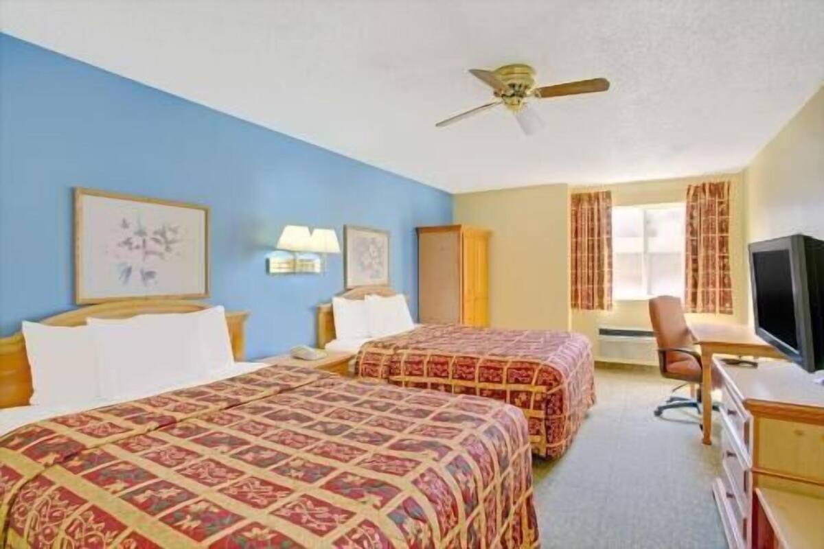 A hotel room with two beds, a desk, a television, and a ceiling fan.