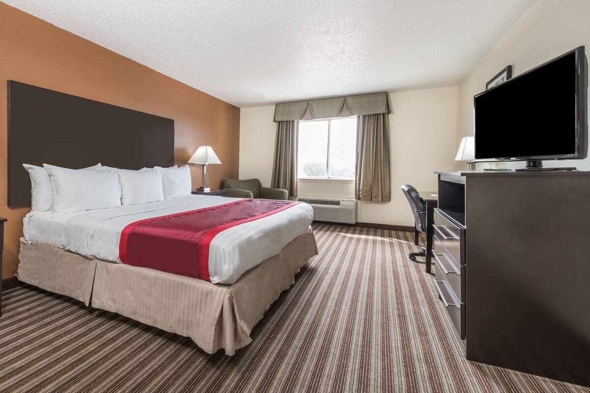 Een hotelkamer met een bed, een bureau, een televisie en een raam met gordijnen.