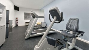 A gym with treadmills, an elliptical, and a chair. - Days Inn & Suites by Wyndham Dallas (Dallas)