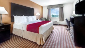 A hotel room with a large bed, a desk with a chair, a TV, and a window with curtains. - Days Inn & Suites by Wyndham Dallas (Dallas)