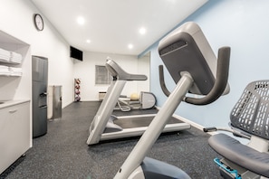 Ein modernes Fitnessstudio mit Laufband, Ergometer und einem wandmontierten Fernseher.
