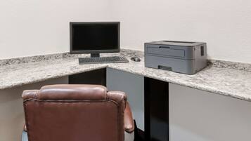 A corner office with a desktop computer, a printer, and a leather chair.